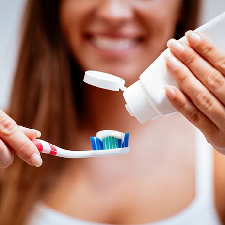 Woman blurry in background squeezing toothpaste onto toothbrush in foreground