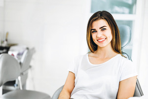 Woman in white shirt sitting in dental chair and smiling